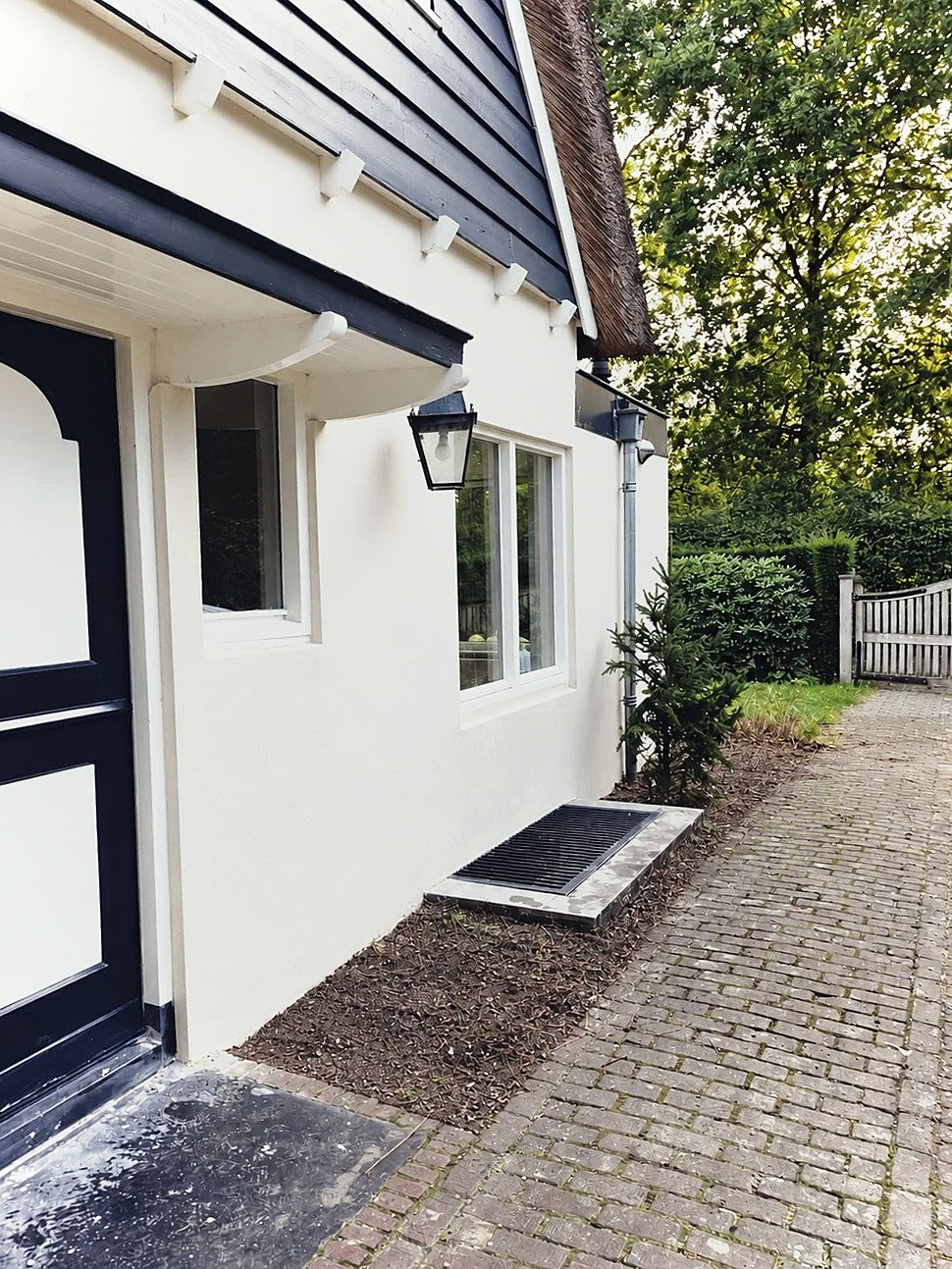 Witte gestucte gevel met donkere houten deur en buitenlamp in Laren