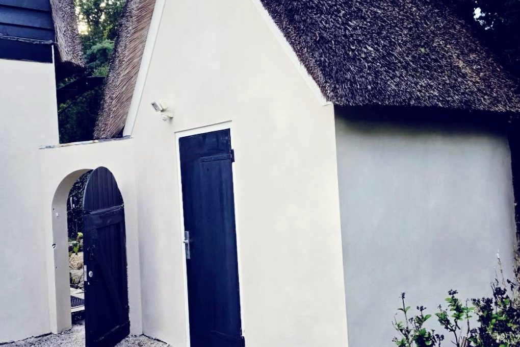 Wit gestucte aanbouw met rieten dak en zwarte deuren in Laren — eigen werkfoto van Renovra Bouw